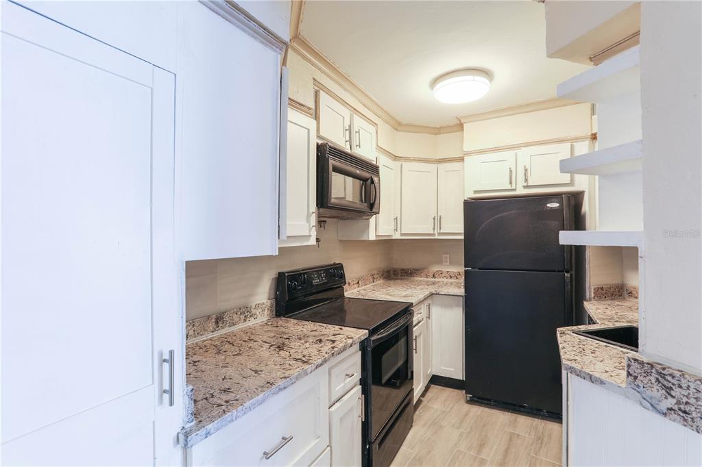 A kitchen features white cabinets, granite countertops, black appliances, and light-colored wood-look flooring — 3655 ATRIUM DRIVE UNIT 2, ORLANDO, FL