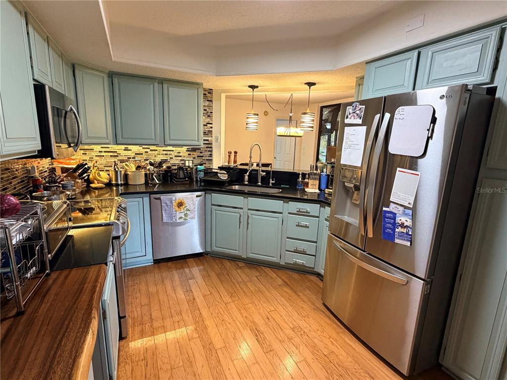 A kitchen features light blue cabinets, stainless steel appliances, and wood flooring — 2823 MARSALA COURT UNIT 2823, ORLANDO, FL