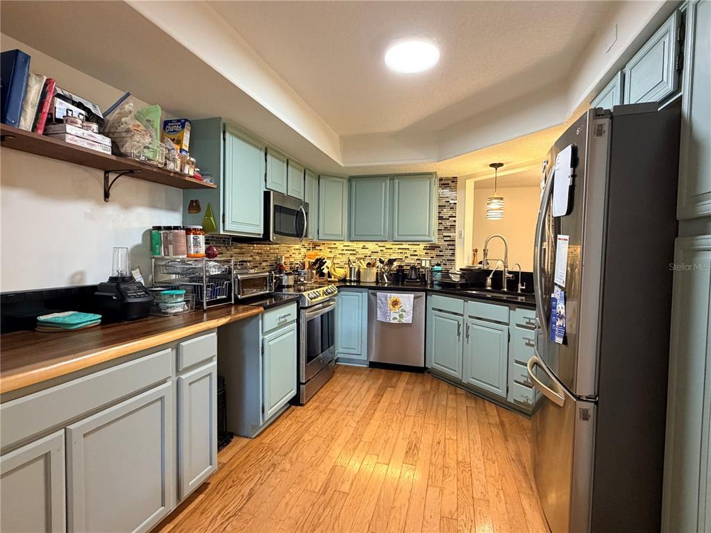 A kitchen features light blue cabinets, stainless steel appliances, and wood flooring — 2823 MARSALA COURT UNIT 2823, ORLANDO, FL