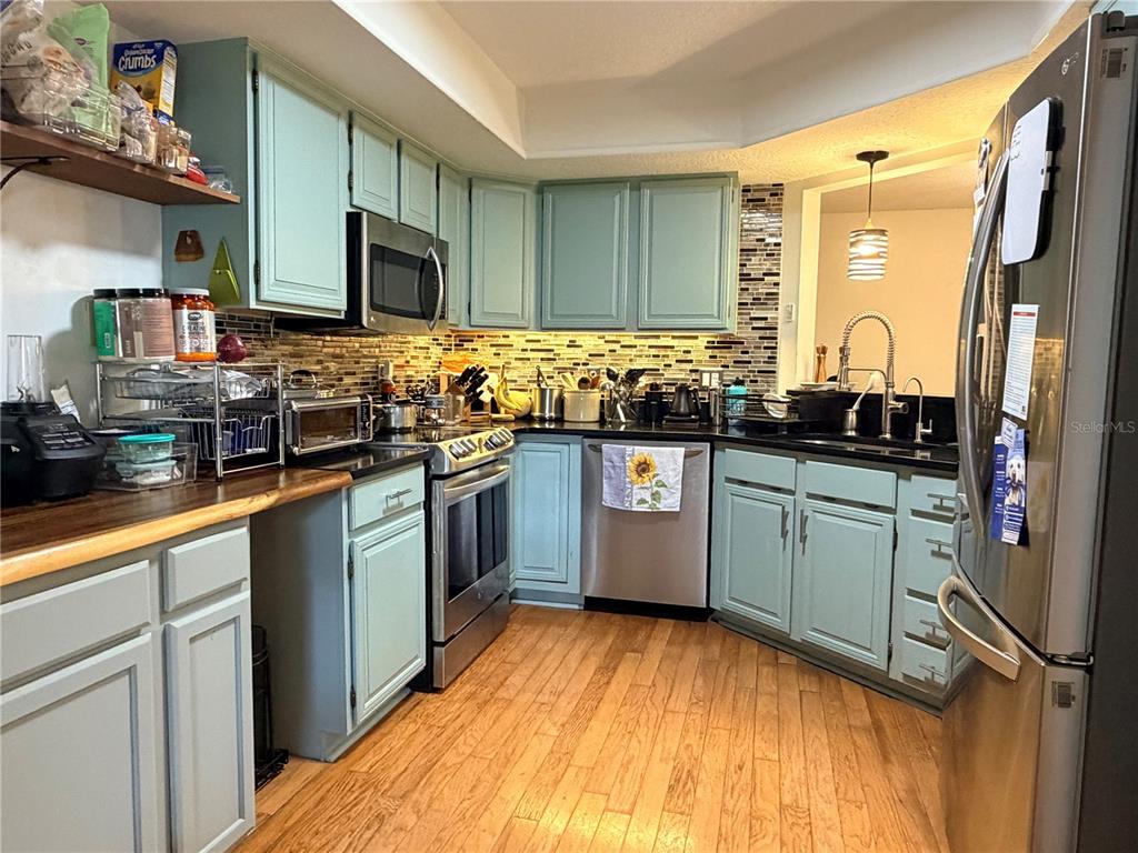 A kitchen features light blue cabinets, stainless steel appliances, a tile backsplash, and wood flooring — 2823 MARSALA COURT UNIT 2823, ORLANDO, FL