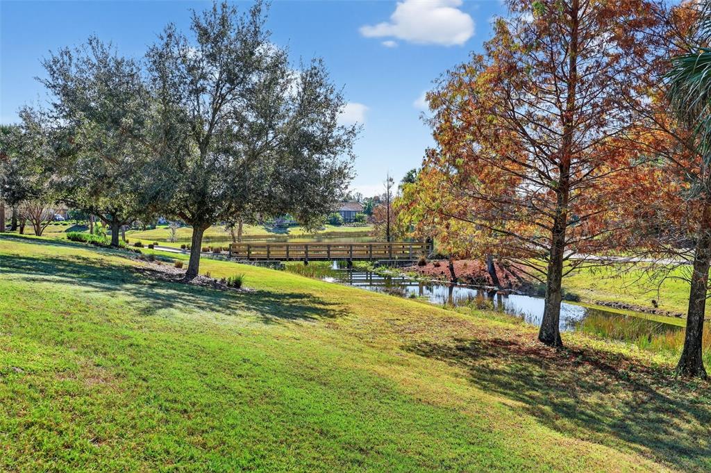 A wooden footbridge crosses a small pond surrounded by grassy lawns and mature trees — 12826 DEL CORSO LOOP, BRADENTON, FL