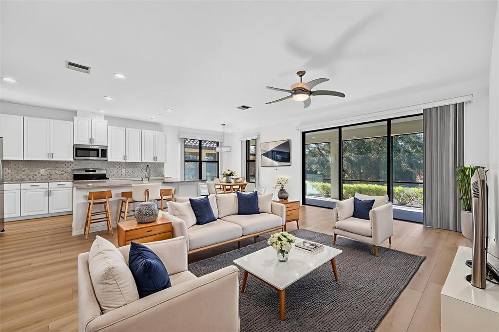 A bright open-concept living room and kitchen feature light wood floors and large sliding doors — 12826 DEL CORSO LOOP, BRADENTON, FL