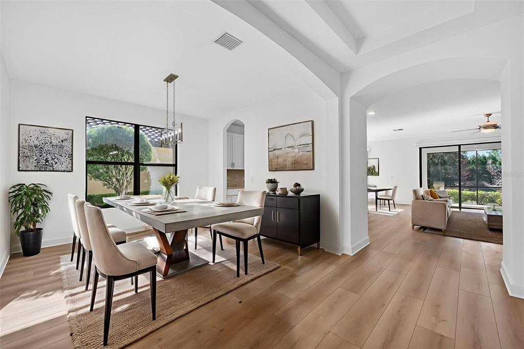 A dining room with a rectangular table and chairs opens into a bright living area — 12826 DEL CORSO LOOP, BRADENTON, FL