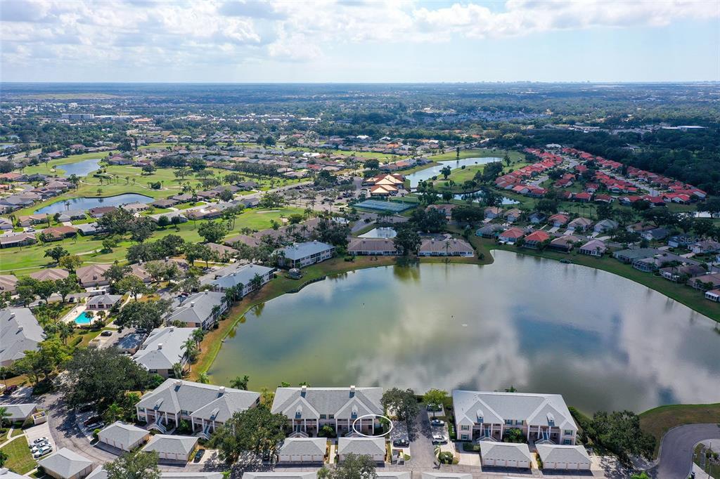 An aerial view shows a residential complex with multi-story buildings surrounding a large lake — 4207 CADDIE DRIVE E UNIT 104, BRADENTON, FL
