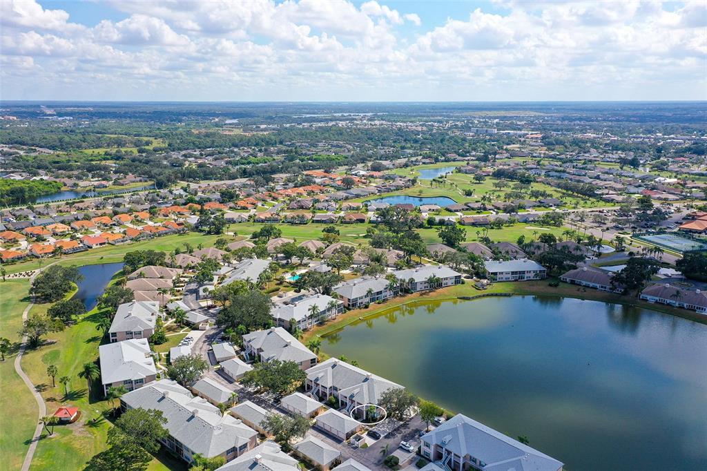 An aerial view shows a residential community with multi-family buildings surrounding a large lake — 4207 CADDIE DRIVE E UNIT 104, BRADENTON, FL