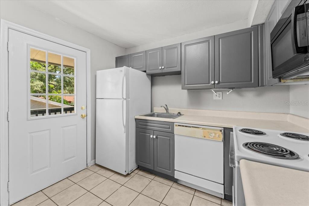 A kitchen features gray cabinets, white appliances, a tiled floor, and a door with glass — 12407 OAK CEDAR PLACE UNIT 202, TAMPA, FL