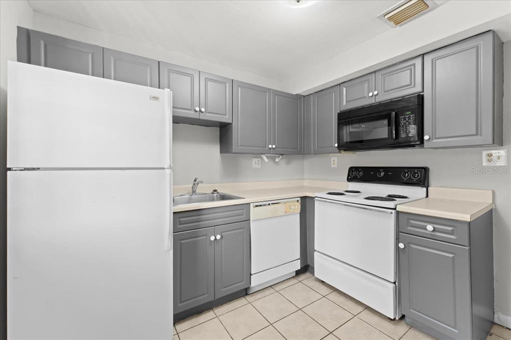 A kitchen features gray cabinets, white appliances, a double-basin sink, and beige tile flooring — 12407 OAK CEDAR PLACE UNIT 202, TAMPA, FL