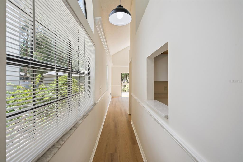 A narrow hallway with light wood flooring, a large window with blinds, and a pass-through opening — 1866 SUMMIT CHASE AVENUE, APOPKA, FL