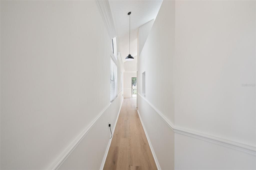 A long hallway features light wood flooring, white walls with chair rail molding, and vaulted ceilings — 1866 SUMMIT CHASE AVENUE, APOPKA, FL