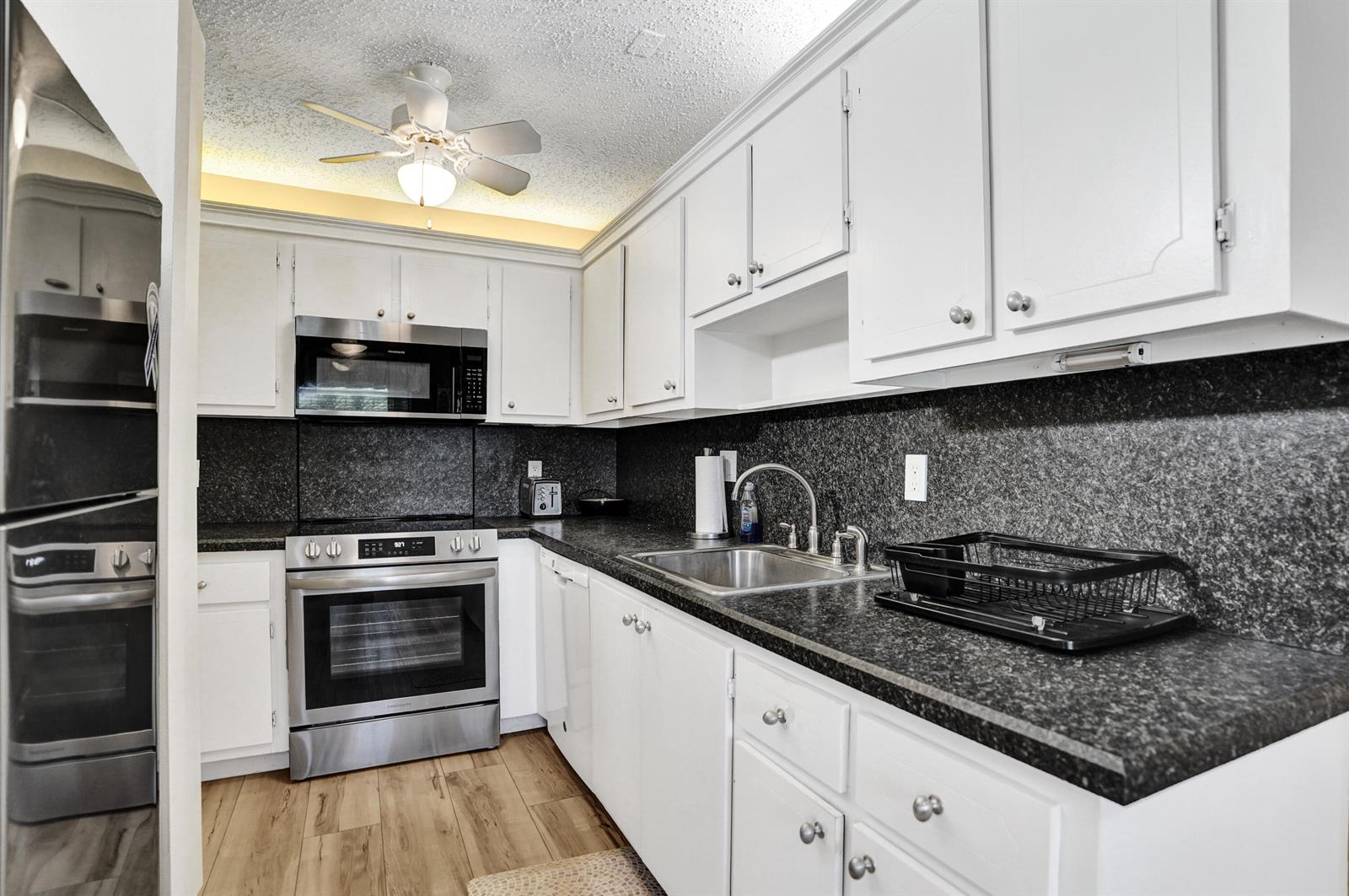 A kitchen features white cabinets, stainless steel appliances, and dark granite countertops — 1050 Citrus Way # 203, Delray Beach FL 33445, DELRAY BEACH, FL