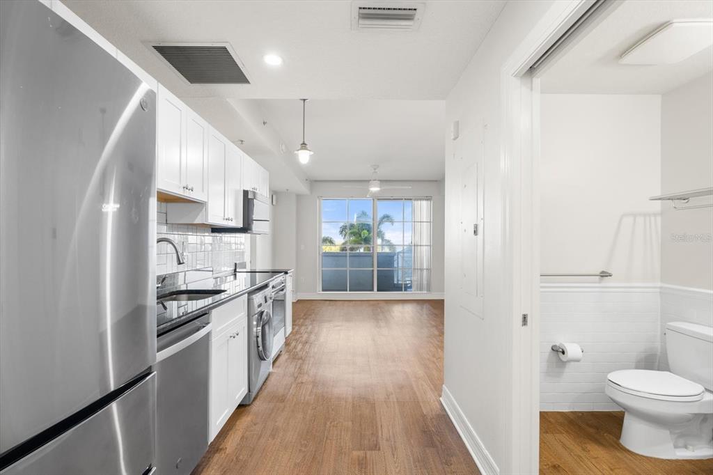 A kitchen with stainless steel appliances and white cabinets opens to a living area — 536 BAHIA BEACH BOULEVARD UNIT 233C, RUSKIN, FL
