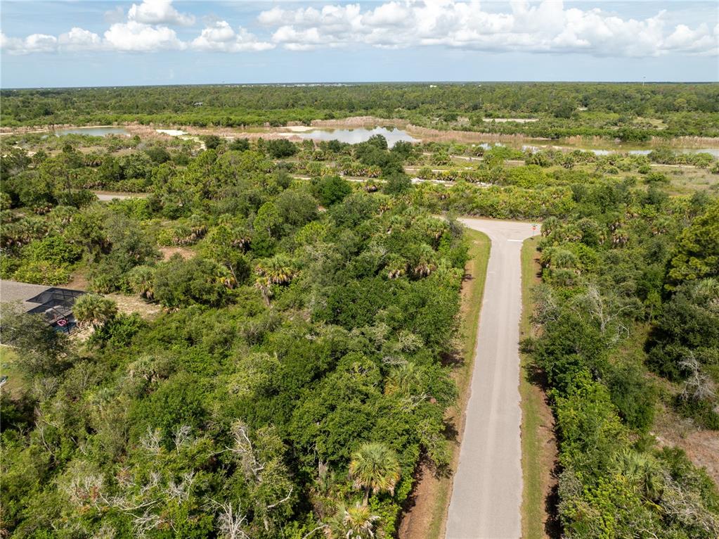 An aerial view shows a paved road leading into a wooded area with a pond — 14427 MOLLA AVENUE, PORT CHARLOTTE, FL