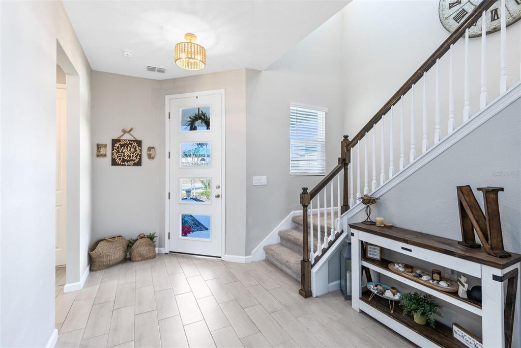 A bright entryway features light wood-look tile flooring, a staircase with white railings, and a door — 4160 SOUTHERN VISTA LOOP, ST CLOUD, FL