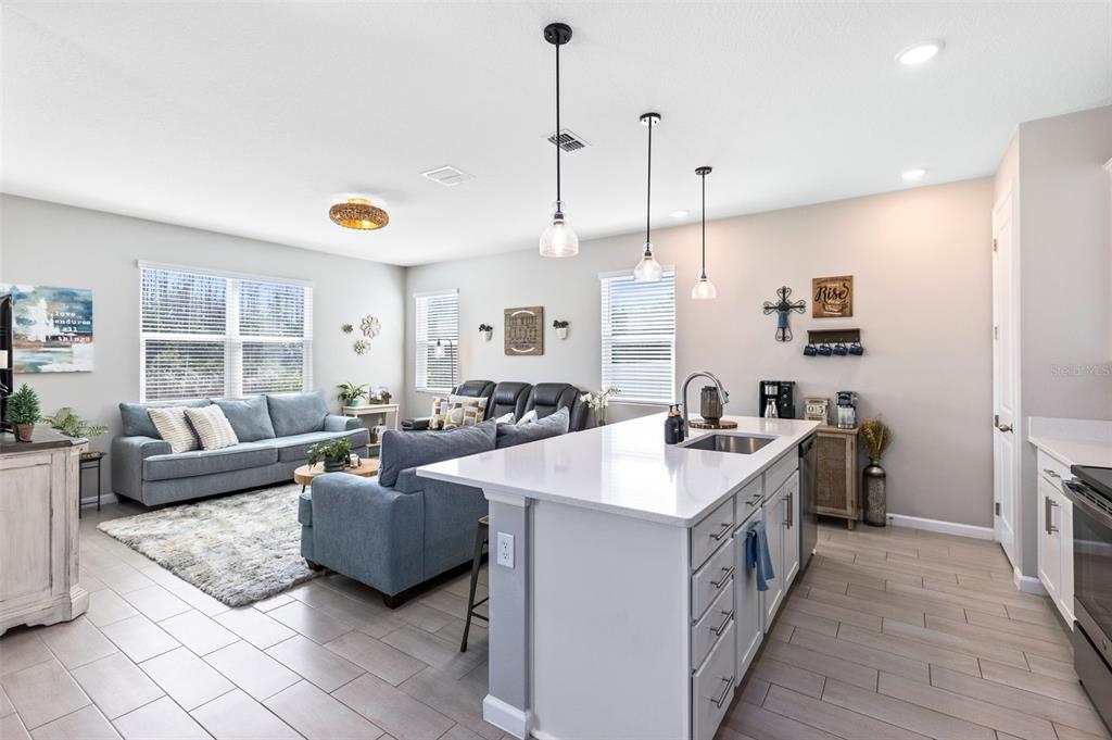 An open-concept kitchen and living area features a large island, gray sofas, and tile flooring — 4160 SOUTHERN VISTA LOOP, ST CLOUD, FL