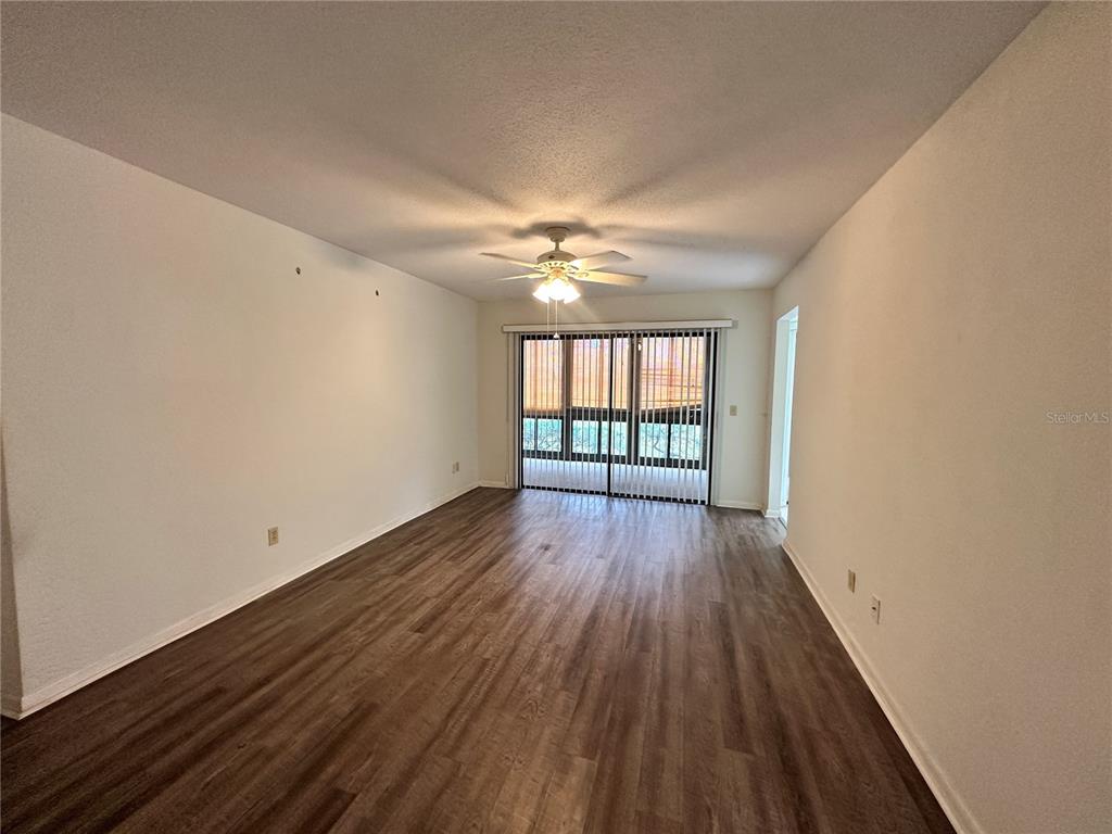 An empty living room features wood-look flooring, a ceiling fan, and sliding glass balcony doors — 13 SURREY COURT UNIT 13, PALM COAST, FL