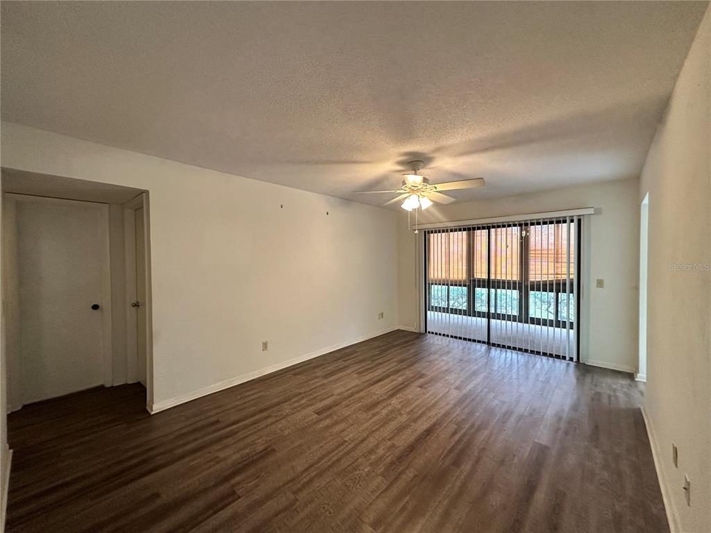 An empty living room features wood-look flooring, a ceiling fan, and sliding glass patio doors — 13 SURREY COURT UNIT 13, PALM COAST, FL