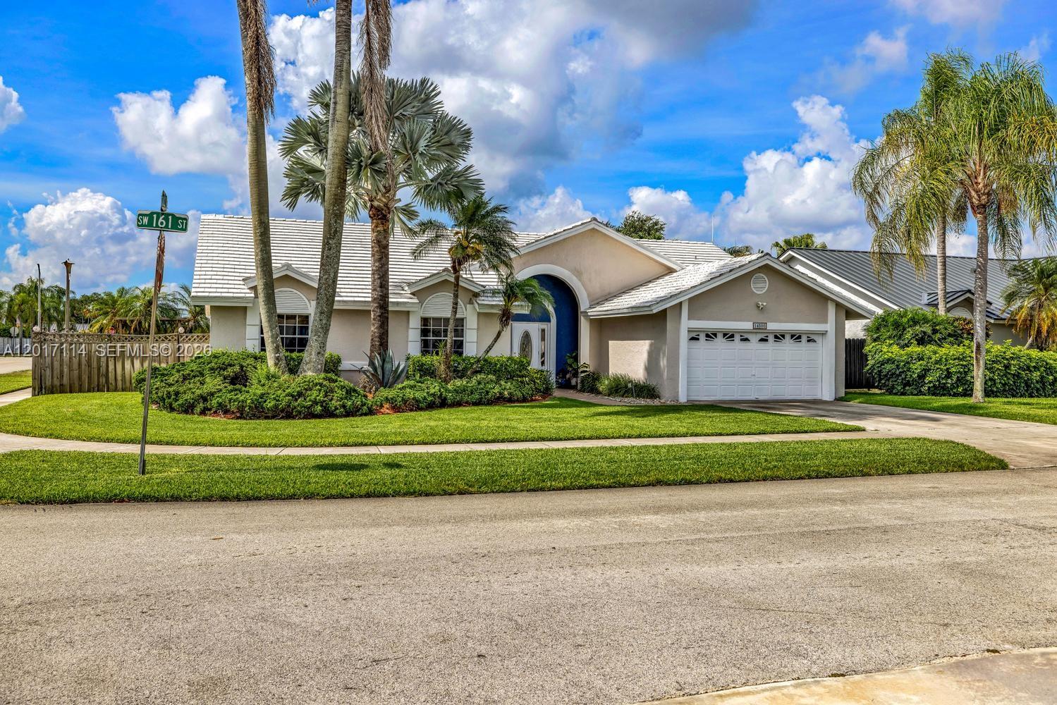 A single-story house with a white tile roof, arched entryway, and palm trees in front — 14500 SW 161st St, Miami FL 33177, MIAMI, FL