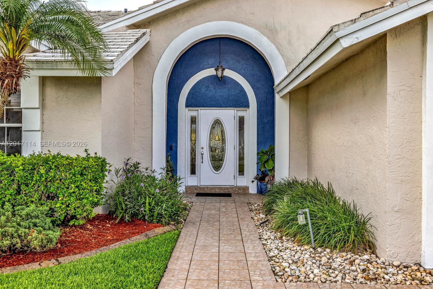 A tiled walkway leads to a white front door framed by a blue arched entryway — 14500 SW 161st St, Miami FL 33177, MIAMI, FL
