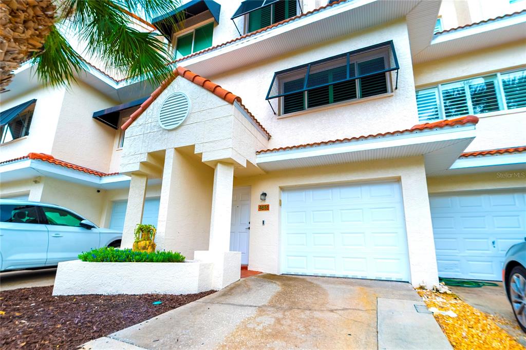 The exterior of a two-story townhouse features a white stucco facade, a garage, and palm trees — 4651 MIRABELLA COURT, ST PETE BEACH, FL