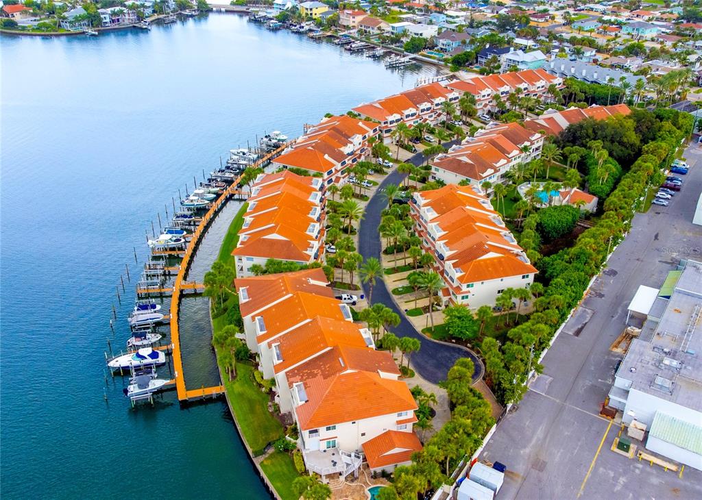 An aerial view shows waterfront townhomes with orange roofs, a boat dock, and a parking lot — 4651 MIRABELLA COURT, ST PETE BEACH, FL