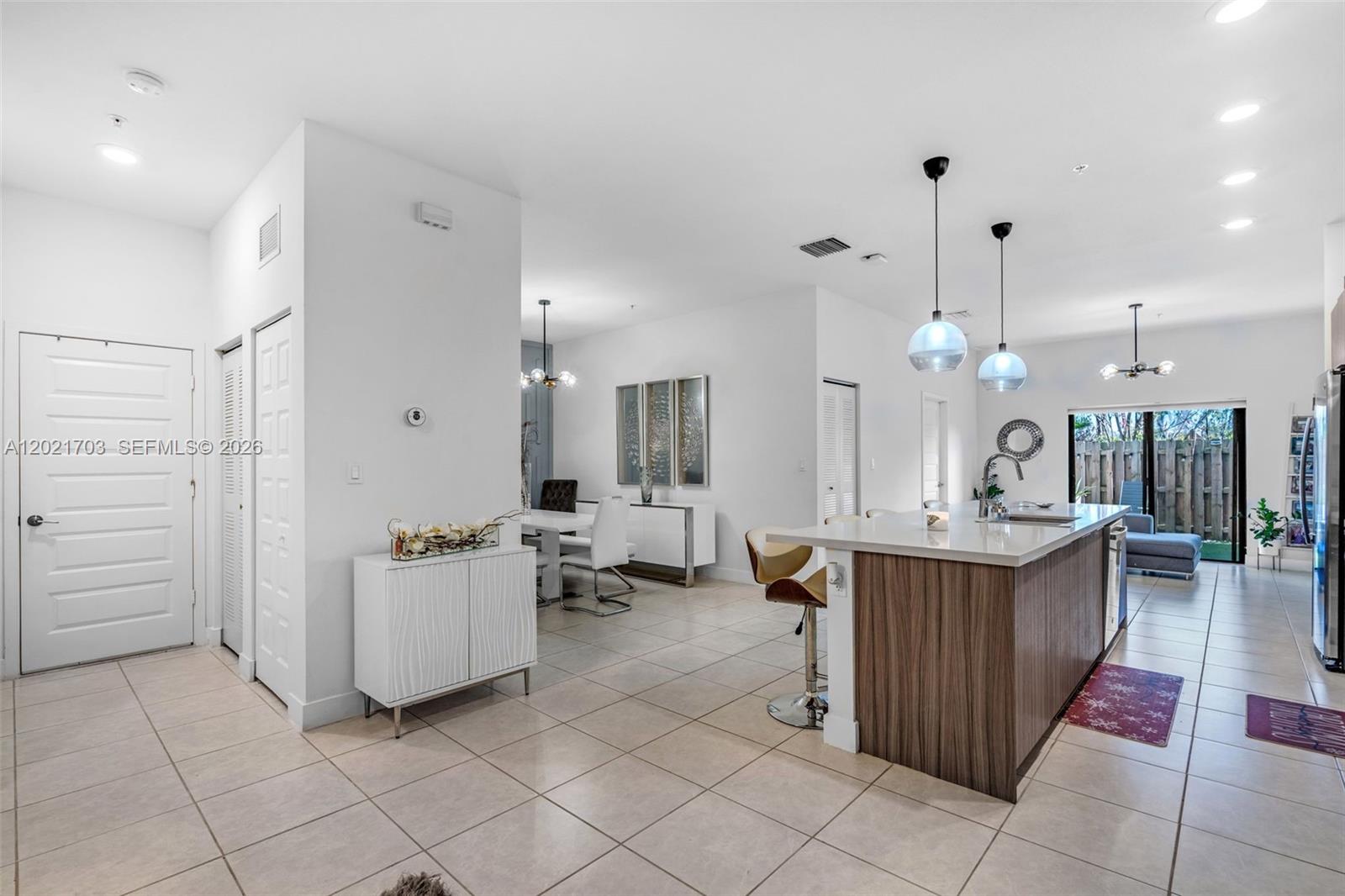 A modern kitchen with a wood-paneled island and pendant lights opens to a dining area — 8015 NW 104th Ave # 3, Doral FL 33178, DORAL, FL