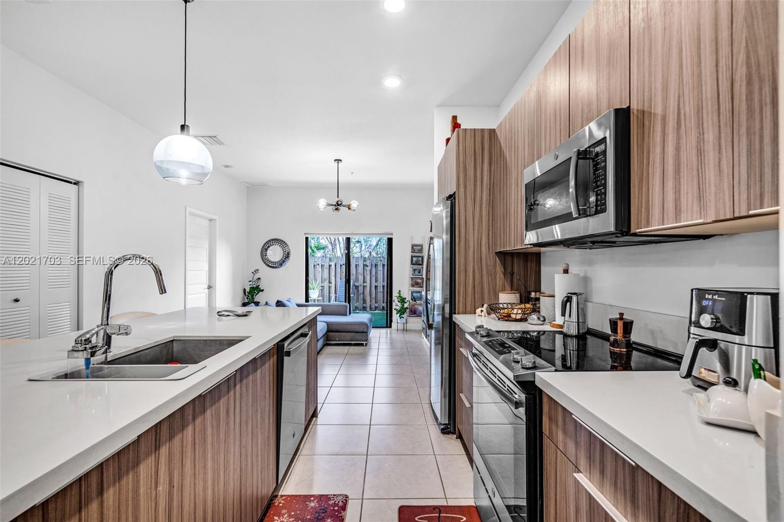 A modern kitchen with wood-grain cabinets and white countertops opens into a living area — 8015 NW 104th Ave # 3, Doral FL 33178, DORAL, FL