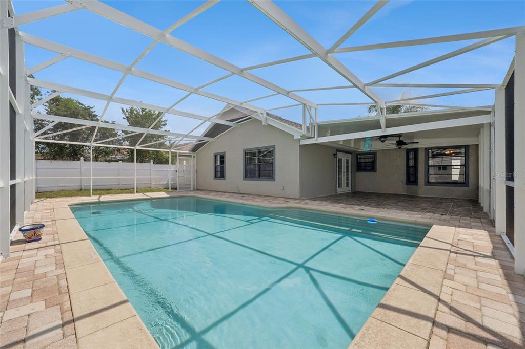 A swimming pool sits inside a screened-in patio area behind a house with gray siding — 2620 E DORCHESTER DR, DELTONA, FL