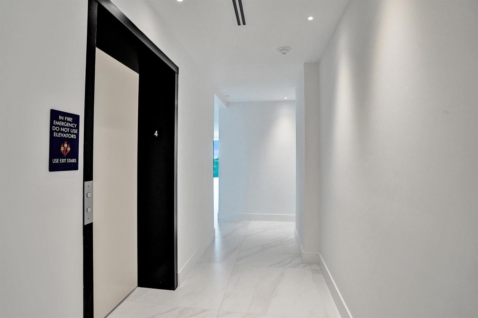 A modern hallway features white tile floors, a white door, and an elevator entrance — 407 N Riverside Drive # 401, Pompano Beach FL 33062, POMPANO BEACH, FL
