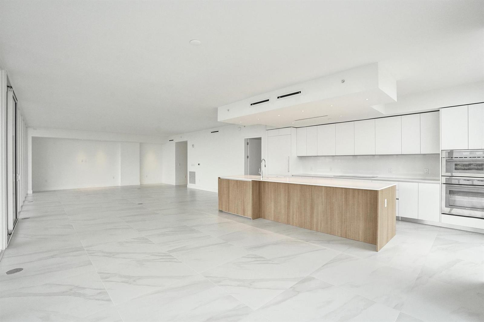 A modern, open-concept kitchen and living area featuring white cabinetry, wood island, and marble flooring — 407 N Riverside Drive # 401, Pompano Beach FL 33062, POMPANO BEACH, FL