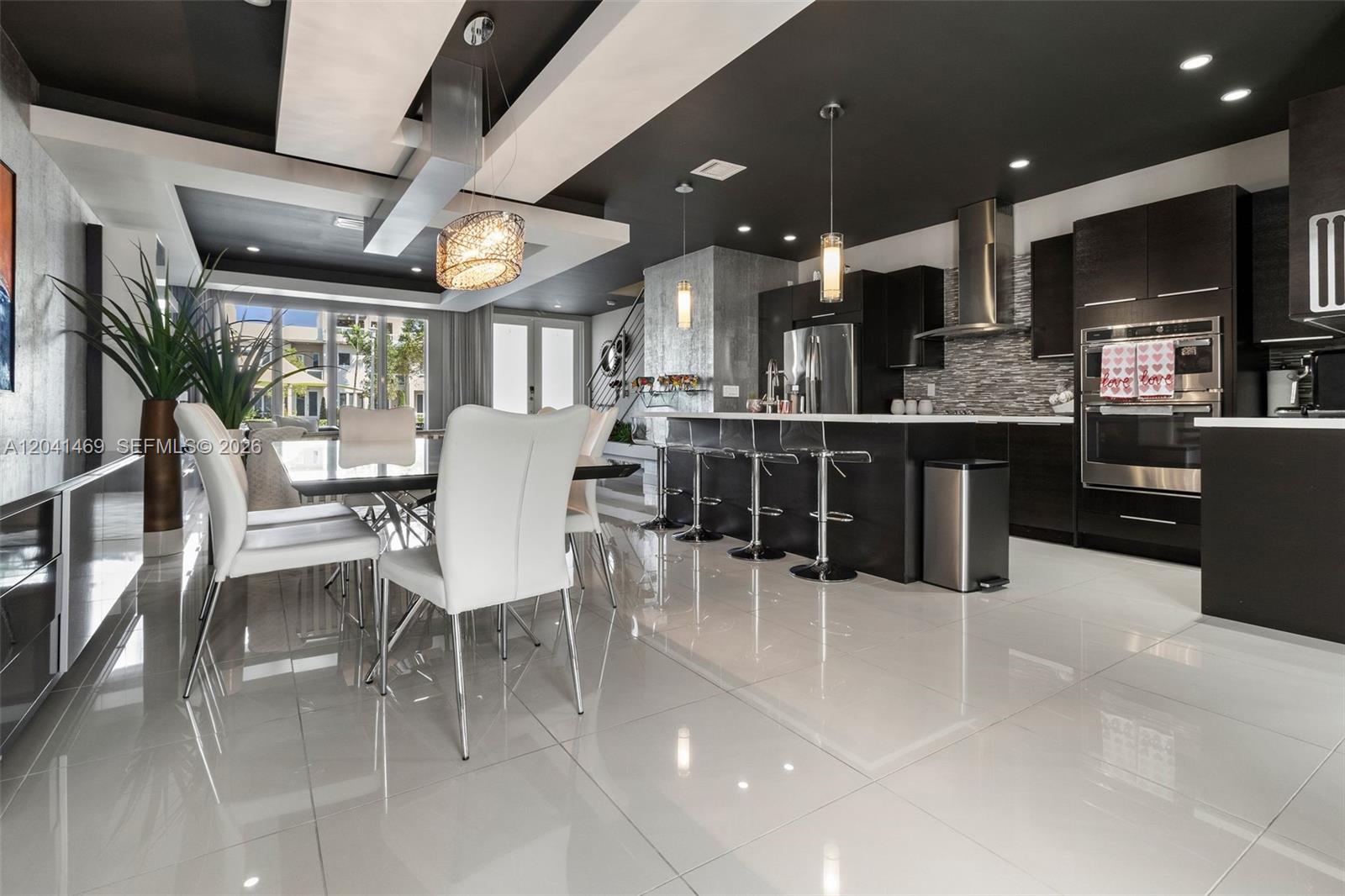 A modern kitchen and dining area feature dark cabinetry, white tile floors, and pendant lighting — 6306 NW 104th Path, Doral FL 33178, DORAL, FL