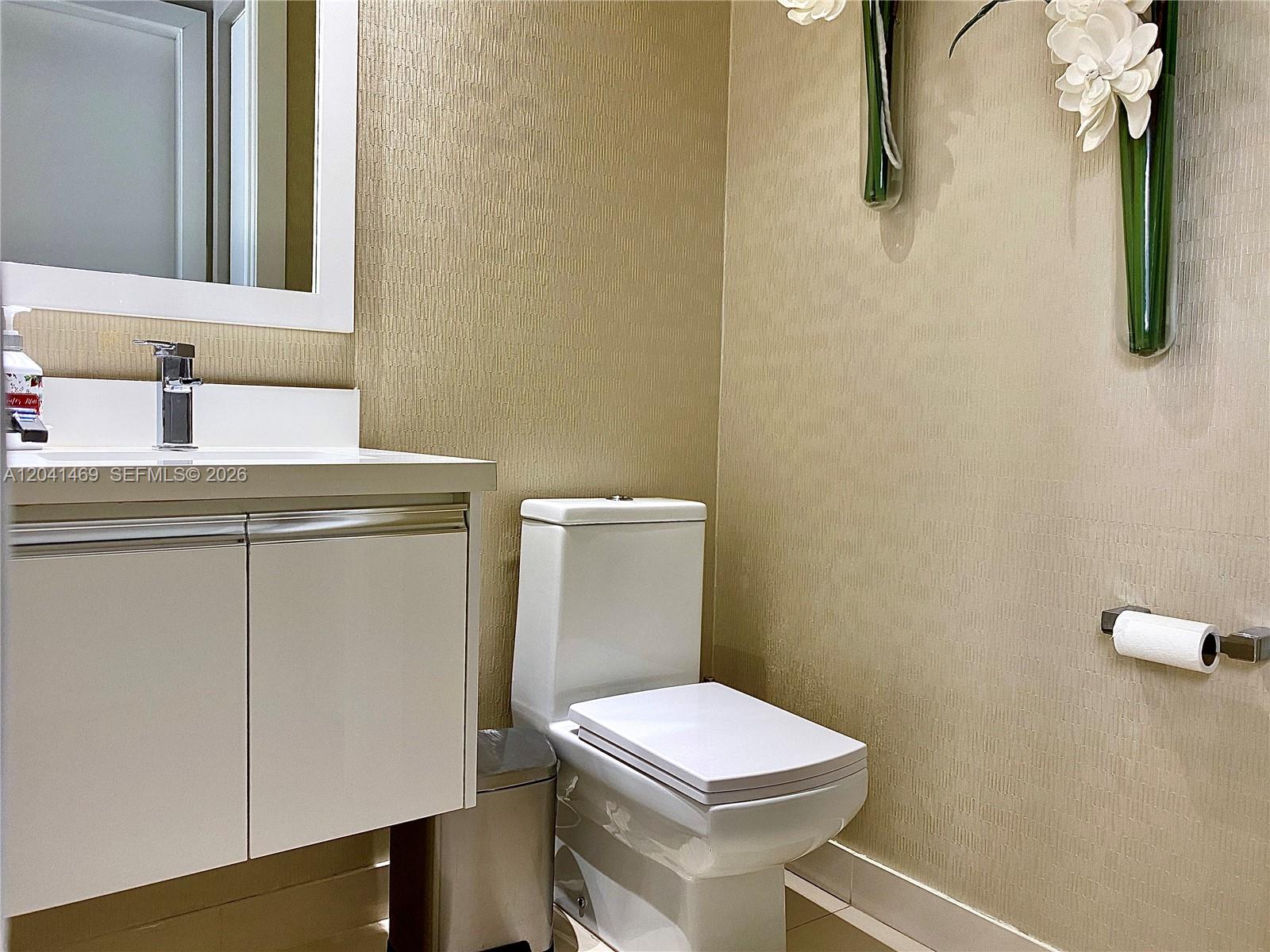 A modern bathroom features a white vanity, a toilet, and textured beige wallpaper — 6306 NW 104th Path, Doral FL 33178, DORAL, FL