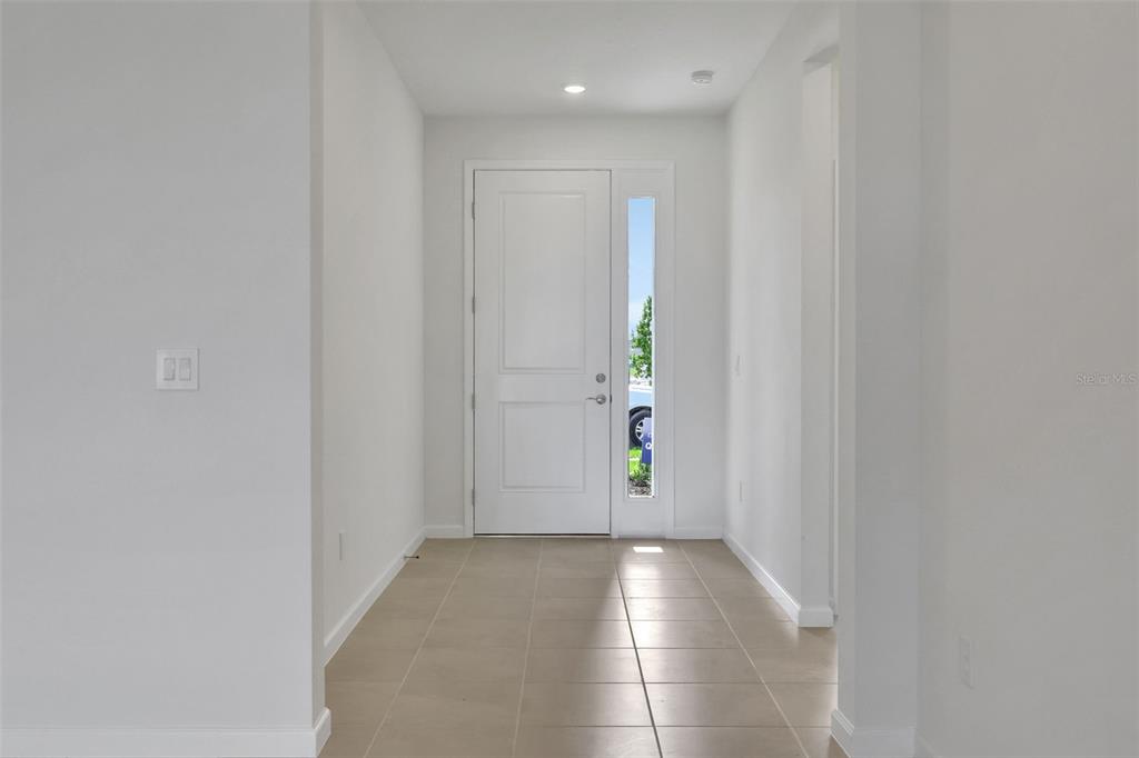 A bright entryway features light tile flooring, white walls, and a door with a sidelight — 10716 NW SUNCREST LOOP, PORT ST LUCIE, FL