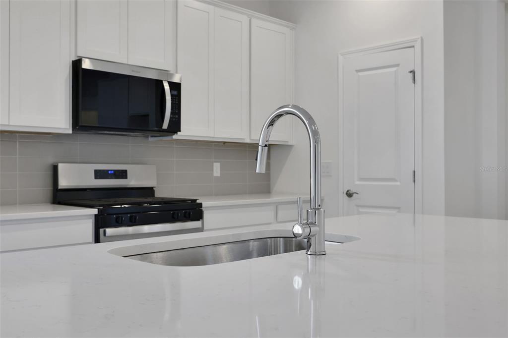 A modern kitchen features white cabinets, stainless steel appliances, and a large quartz-topped island — 10716 NW SUNCREST LOOP, PORT ST LUCIE, FL
