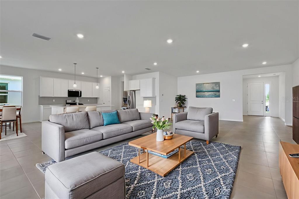 An open-concept living room features a grey sofa, a coffee table, and a kitchen area — 10716 NW SUNCREST LOOP, PORT ST LUCIE, FL