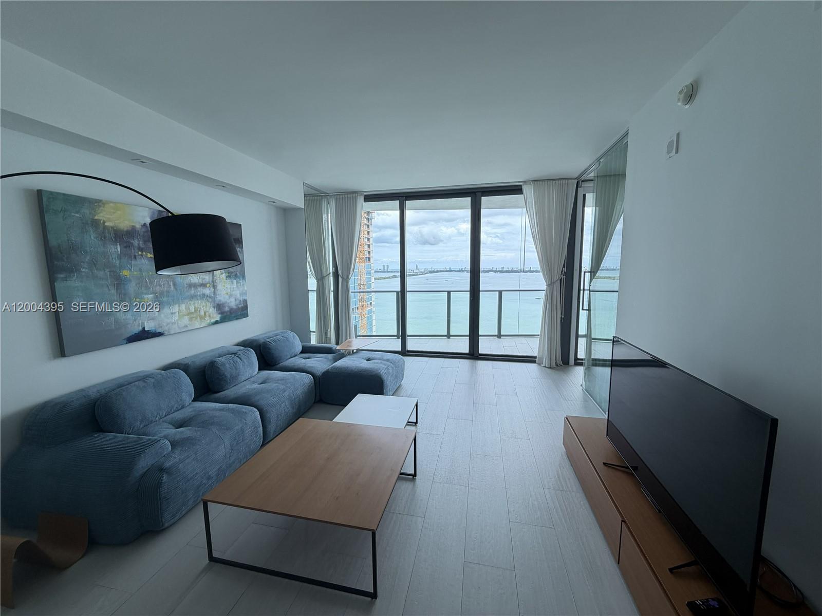 A modern living room features a blue sectional sofa, wood coffee tables, and floor-to-ceiling windows — 460 NE 28th St # 2806, Miami FL 33137, MIAMI, FL