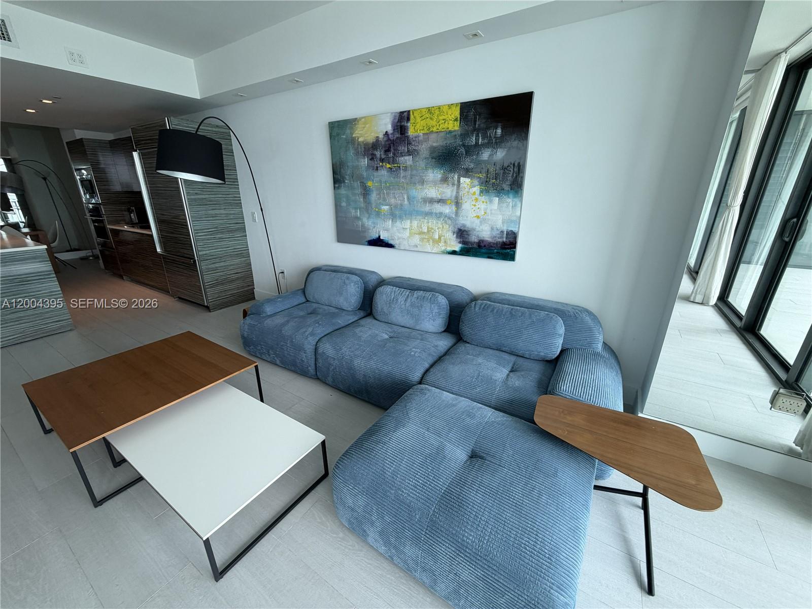 A modern living room features a blue corduroy sectional, nested coffee tables, and abstract art — 460 NE 28th St # 2806, Miami FL 33137, MIAMI, FL
