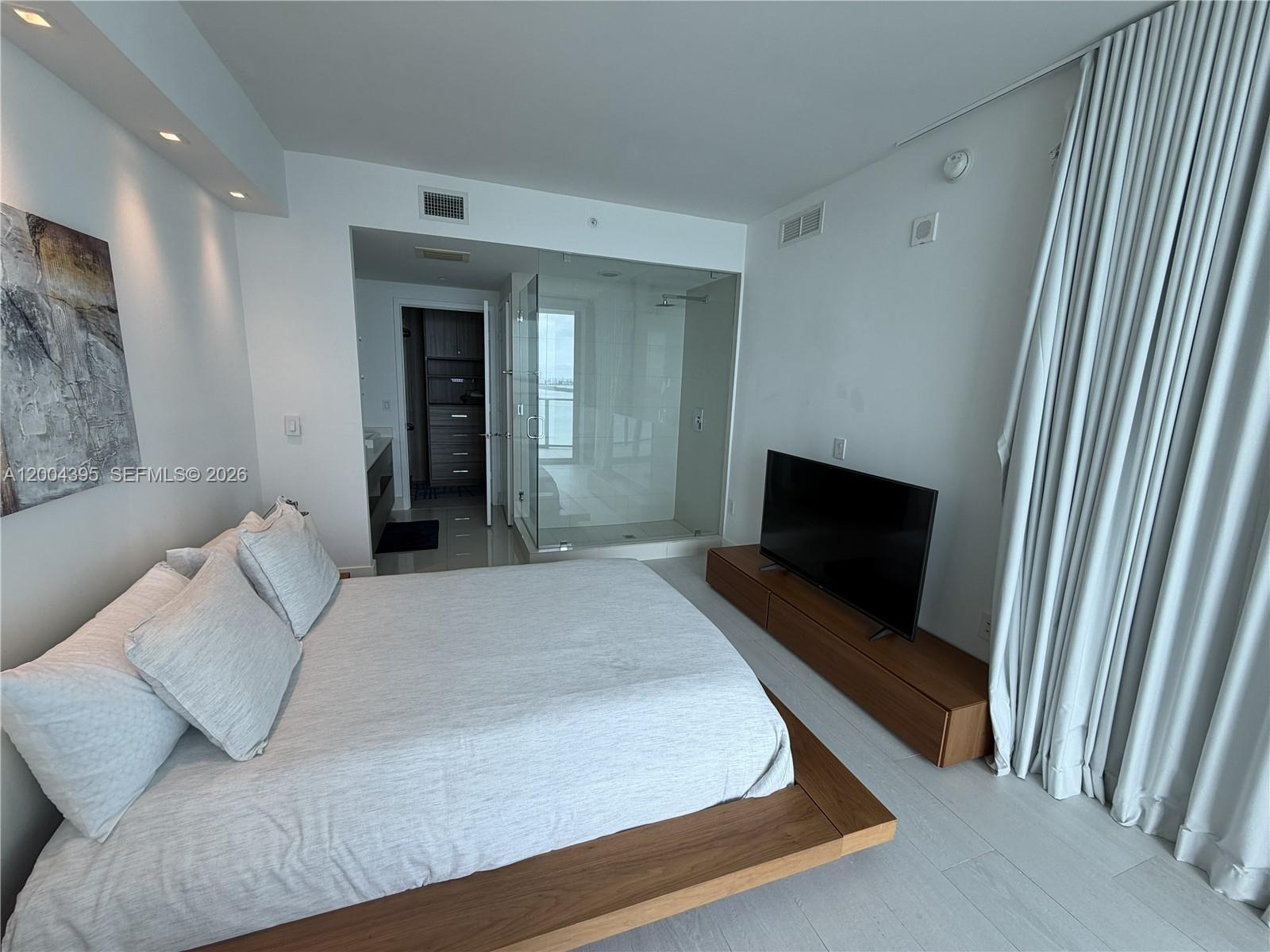 A modern bedroom features a platform bed, a glass-enclosed shower, and a television console — 460 NE 28th St # 2806, Miami FL 33137, MIAMI, FL
