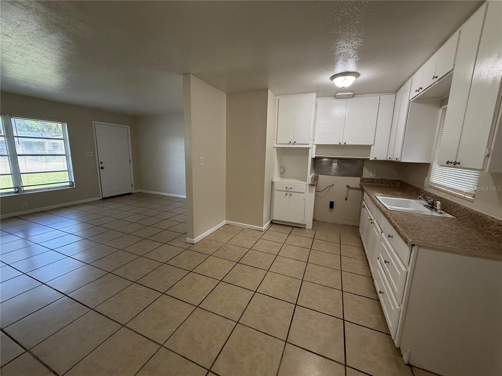 A kitchen with white cabinets and tile flooring opens into a living area with a door — 1323 BRAEBURY DRIVE, LEESBURG, FL