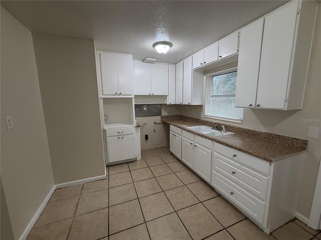 A kitchen features white cabinets, a speckled countertop, a sink, and tiled flooring — 1323 BRAEBURY DRIVE, LEESBURG, FL