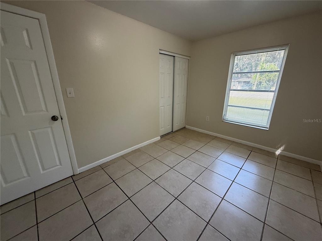 An empty bedroom features beige walls, light-colored floor tiles, a window, and a sliding closet — 1323 BRAEBURY DRIVE, LEESBURG, FL