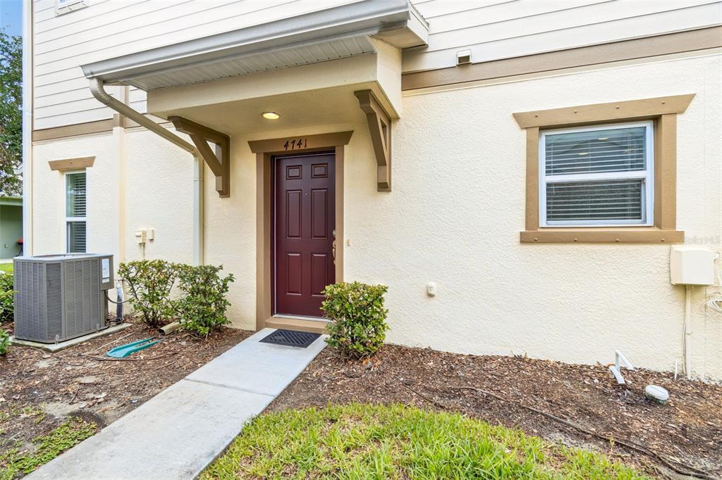 A tan stucco building exterior features a maroon front door and a concrete walkway — 4741 CHATTERTON WAY, RIVERVIEW, FL