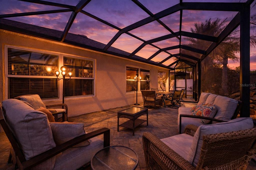 A screened-in patio features wicker furniture, a stone paver floor, and a sunset view — 2859 RESMONDO ROAD, THE VILLAGES, FL