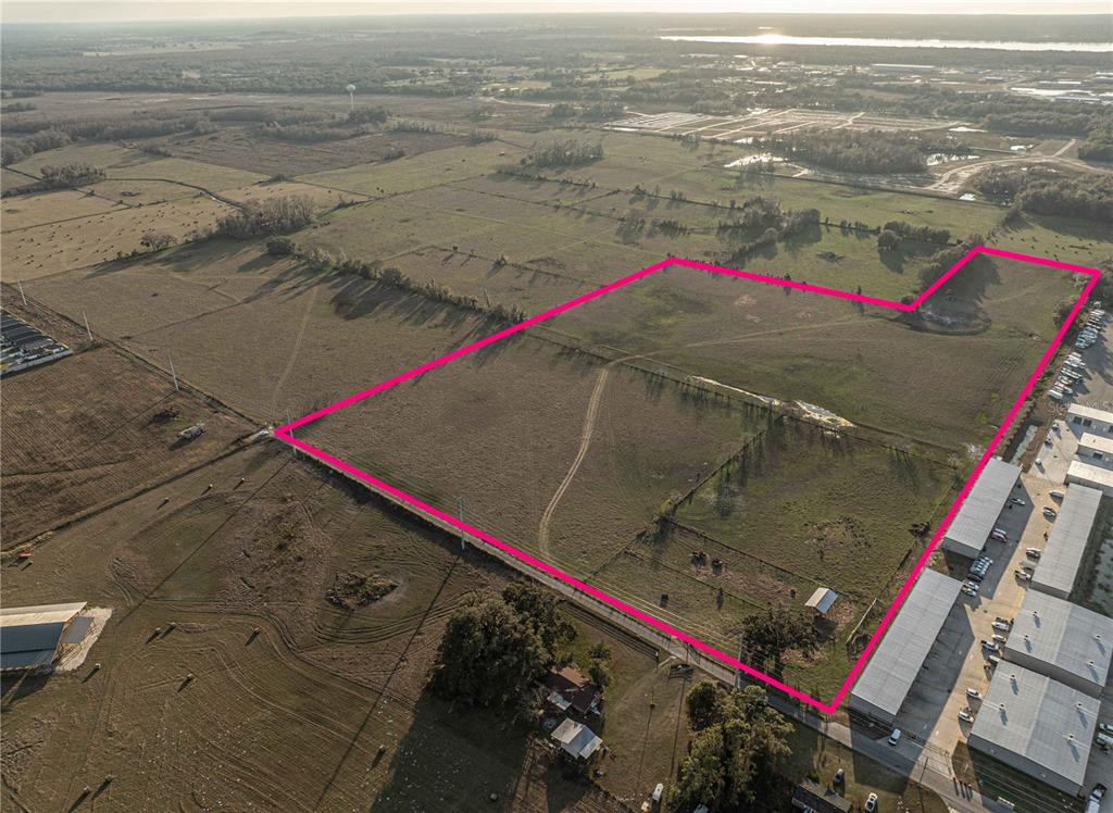 An aerial view shows a large, open grassy lot outlined in pink next to industrial buildings — CR 523, WILDWOOD, FL