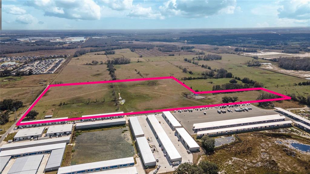 An aerial view shows a large, vacant grassy lot outlined in pink behind a storage facility — CR 523, WILDWOOD, FL