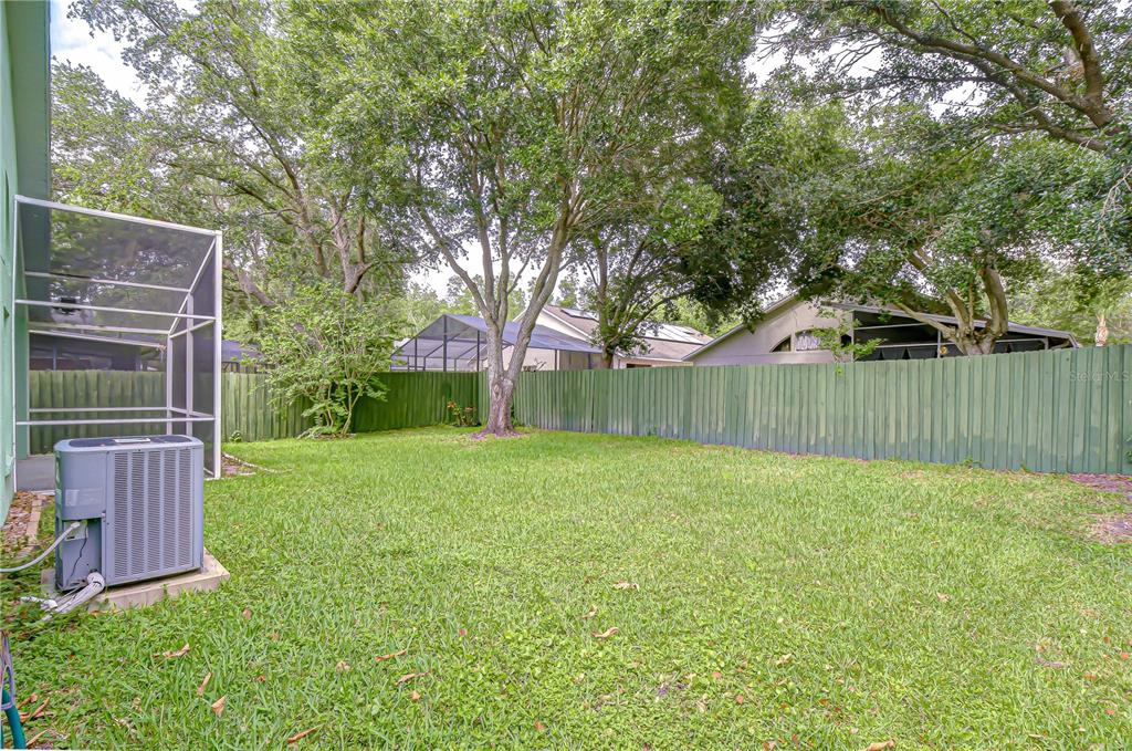 A fenced backyard features a grassy lawn, mature trees, and an outdoor air conditioning unit — 18927 TWINBERRY DRIVE, TAMPA, FL
