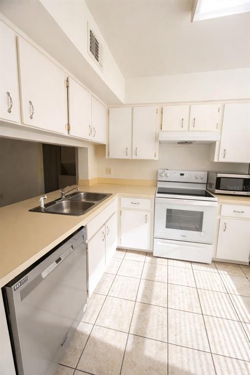 A kitchen with white cabinets, a stainless steel dishwasher, and a white electric range — 3244 CANDLE RIDGE DRIVE UNIT 202, ORLANDO, FL
