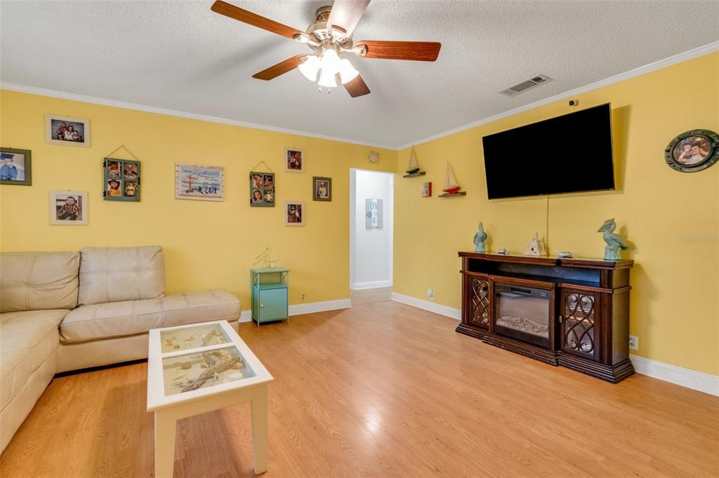 A living room with yellow walls, wood-look flooring, a ceiling fan, and a television console — 202 SAINT LUCIE ROAD, WINTER HAVEN, FL