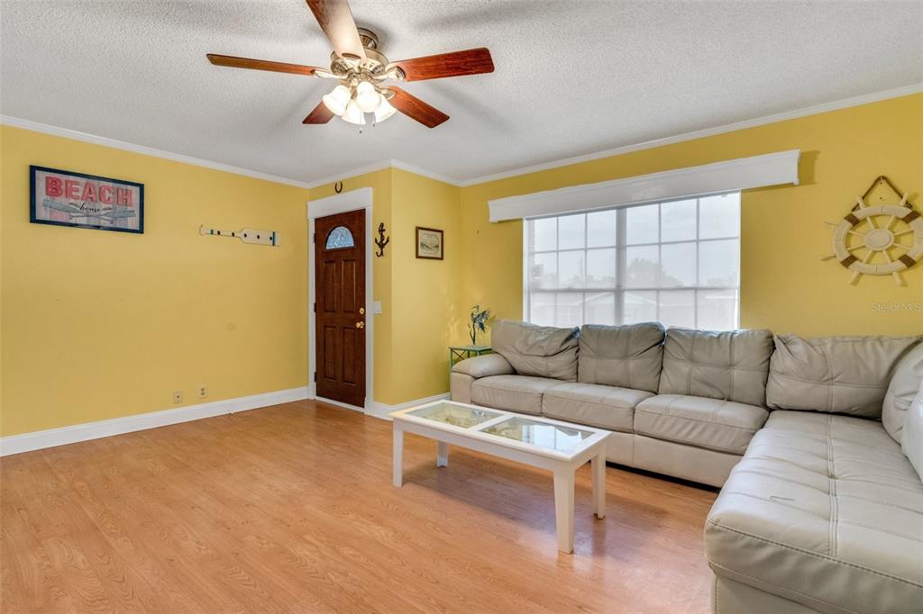 A living room features yellow walls, wood-look flooring, a white sectional sofa, and a ceiling fan — 202 SAINT LUCIE ROAD, WINTER HAVEN, FL