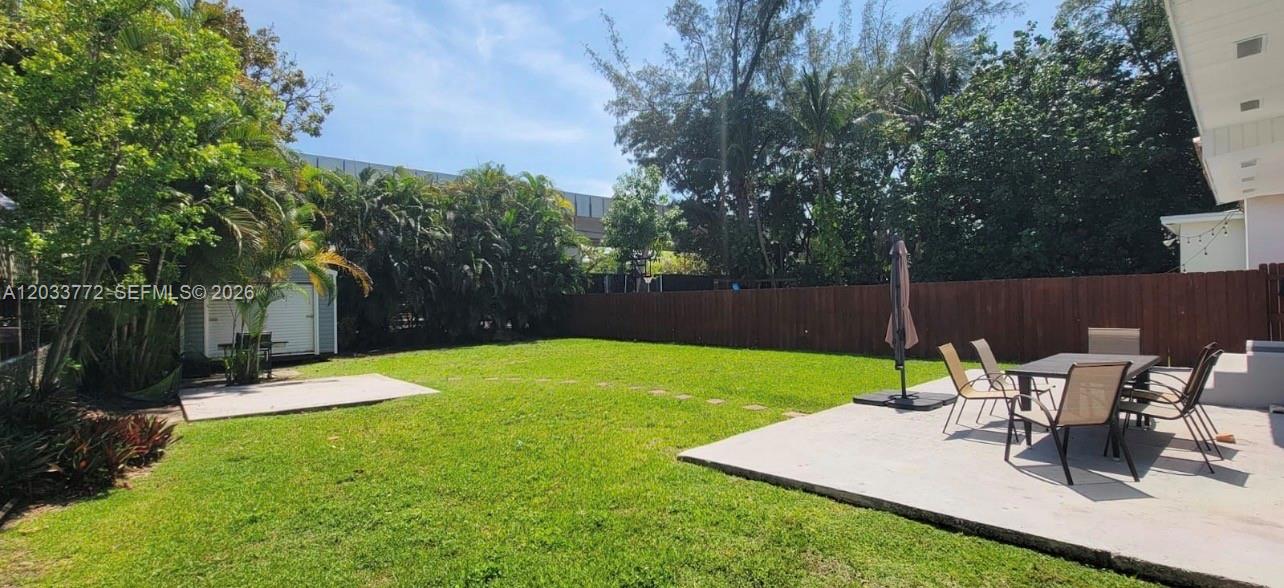 A grassy backyard features a concrete patio with outdoor dining furniture and a wooden fence — 3685 SW 1st Ave, Miami FL 33145, MIAMI, FL