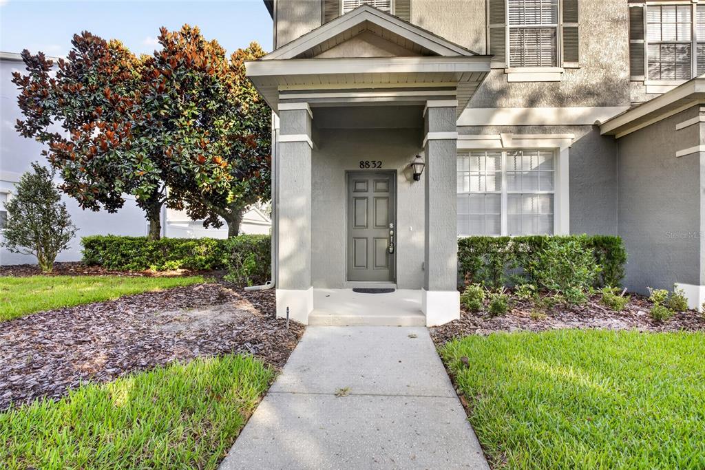 A concrete walkway leads to the covered front entrance of a two-story gray house — 8832 DANFORTH DRIVE, WINDERMERE, FL